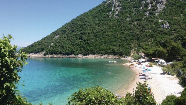 A beach with clear turquoise water, surrounded by lush green hills.