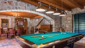 A pool table labeled "Olympic II" in a room with stone walls, wooden beams, and a chandelier.
