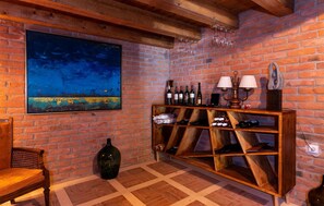 Exposed brick walls and wooden beams create a cozy atmosphere, featuring a large abstract painting and a wine rack with wine bottles.