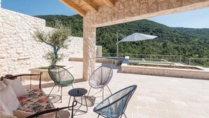 An outdoor patio with stone walls, a wooden ceiling, and a view of a mountainous landscape.