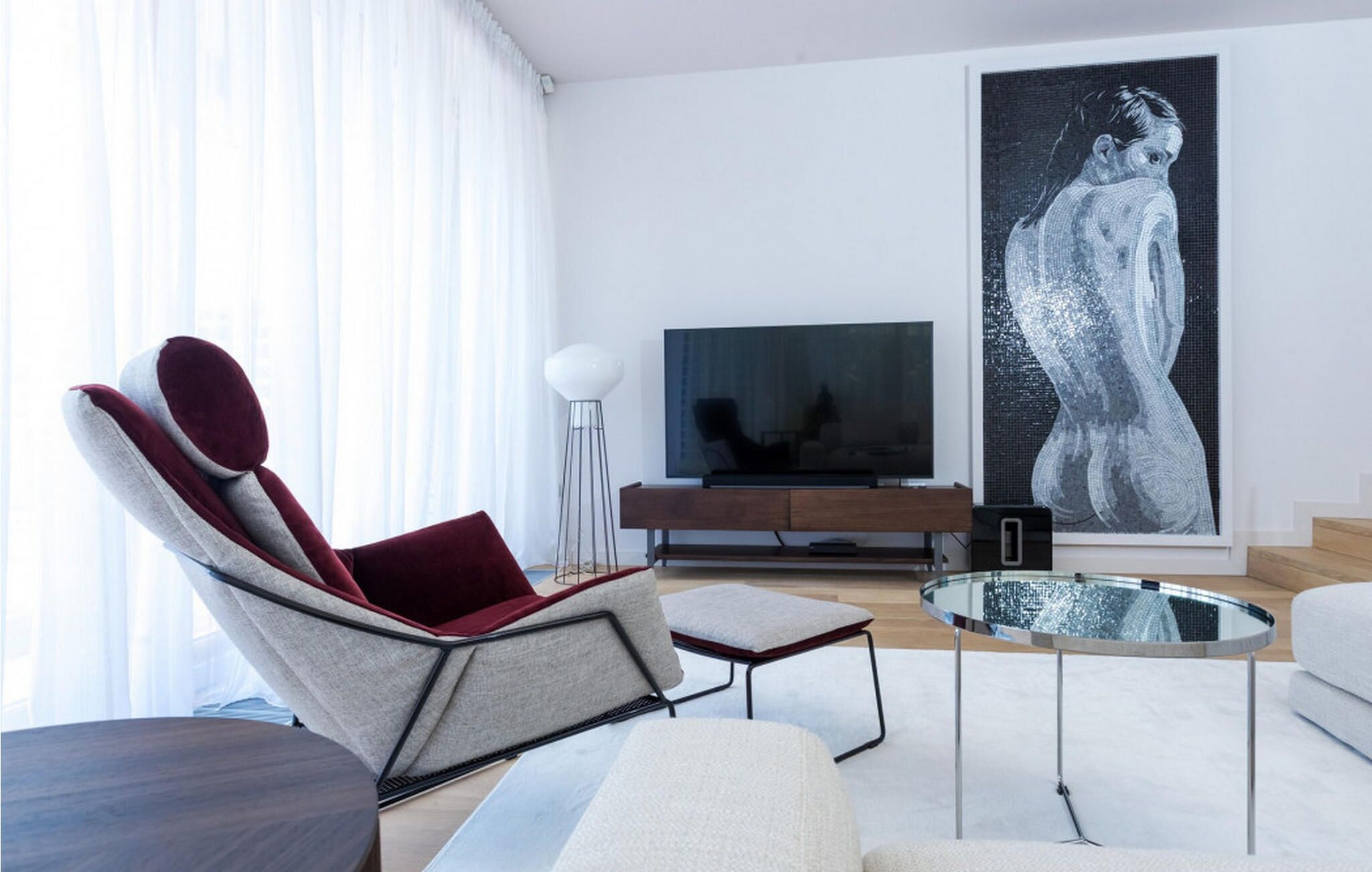 A modern living room with a curved sofa, a glass coffee table, a flat-screen TV, and a large abstract painting.