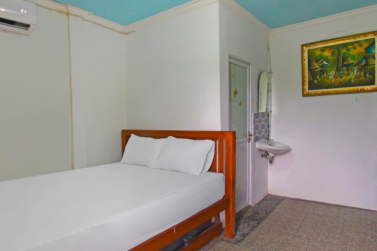 A single bed with a wooden frame and white bedding in a room with white walls, a white ceiling, and a painting on the wall.
