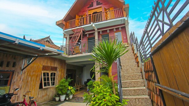 A two-story wooden house with a balcony, potted plants, and a staircase leading to the upper floor. - Hotel O Bale Datu Homestay Near Lapangan Bulutangkis By'u Badminton (Senggigi)