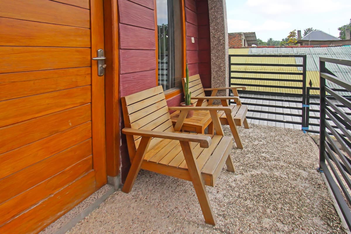 A wooden door with a metal handle, a window with a view of a building, and a gravel patio with two wooden benches.