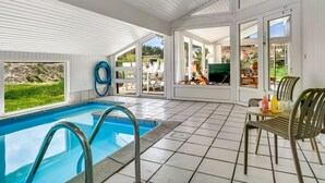 A pool area with a clear view of the outdoors, a pool with a blue color, and a chair with a bottle on the table. - "Gladis" - 900m from the sea by Interhome (Saltum)