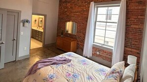 Een slaapkamer met een bakstenen muur, een bed met bloemenbedrukking, een kast en een raam met gordijnen.