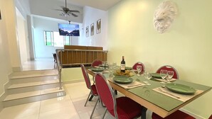 A dining area with a long table set for four, red chairs, and a television in the background.