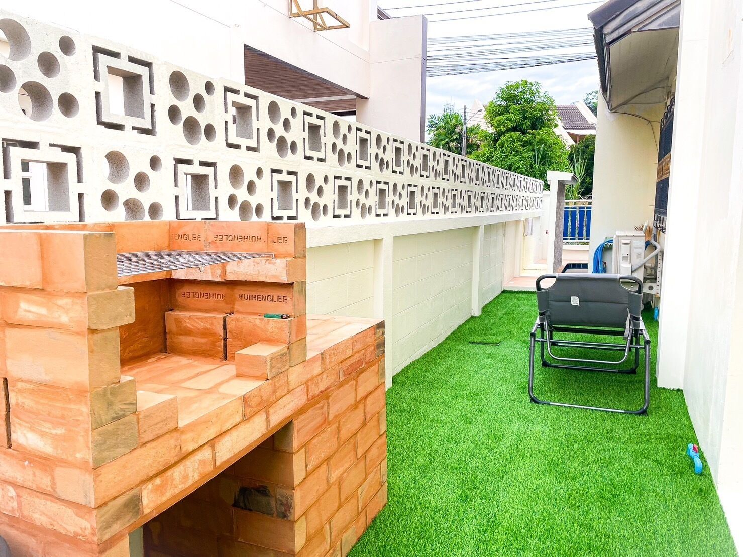 A patio area with a brick barbecue grill, a white decorative wall with geometric cutouts, and artificial green grass.
