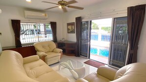 A living room with a ceiling fan, a sofa, a glass coffee table, and a view of a swimming pool through a sliding glass door.