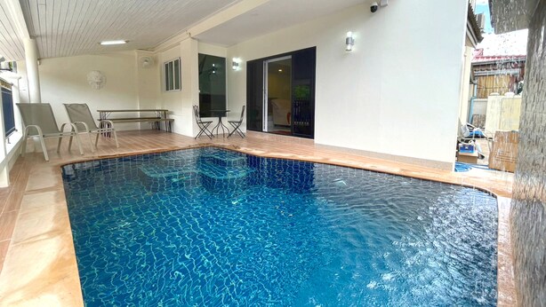 An indoor swimming pool with a tiled floor, a ceiling with a wooden pattern, and a seating area with chairs and a table.