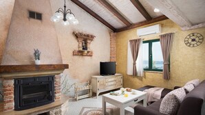 Un salon chaleureux avec une cheminée, un téléviseur et une vue sur la mer par la fenêtre.