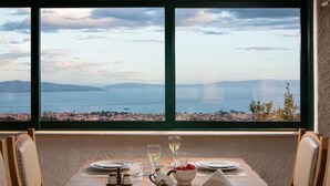 Une table à manger dressée pour deux personnes, avec vue sur un paysage côtier par une grande fenêtre.