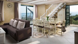 Un salon avec un canapé marron, une table à manger avec des chaises, une grande fenêtre avec des rideaux, un escalier et une vue sur l’extérieur.