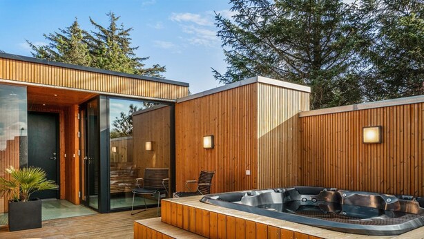 A modern outdoor hot tub area with wooden decking and a glass door entrance.
