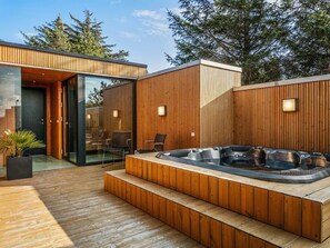 Een moderne buitenjacuzzi met houten terras en glazen toegang.