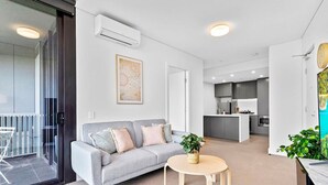 Una sala de estar moderna con un sofá gris, una mesa de centro redonda y una cocina al fondo.