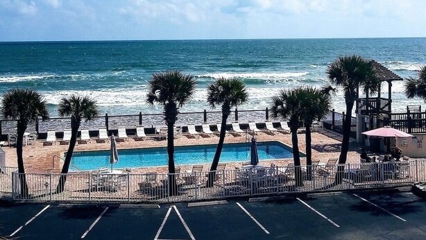 A beachside pool area with lounge chairs and a swimming pool, overlooking the ocean. - Salty ~ Tides Studio Condo near the Beach  (Daytona Beach)