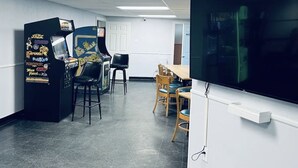 A room with arcade games, a TV, and a dining area. - Salty ~ Tides Studio Condo near the Beach  (Daytona Beach)