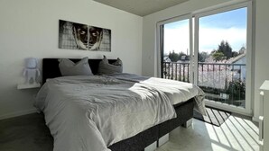 A bedroom with a large bed, a window with a view of a garden, and a ceiling light. - M Apartment: Design Apartment Loft (Landau in der Pfalz)