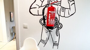 A wall with a black and white astronaut drawing, a fire extinguisher, and a white chair. - M Apartment: Design Apartment Loft (Landau in der Pfalz)