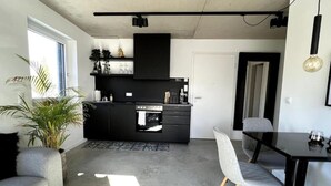 A modern kitchen with black cabinetry, a built-in oven, and a dining area with a table and chairs. - M Apartment: Design Apartment Loft (Landau in der Pfalz)