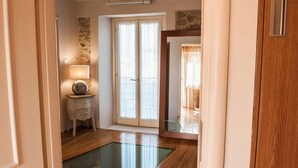 A hallway with a glass table, a lamp, a small wooden cabinet, and a door leading to a balcony.