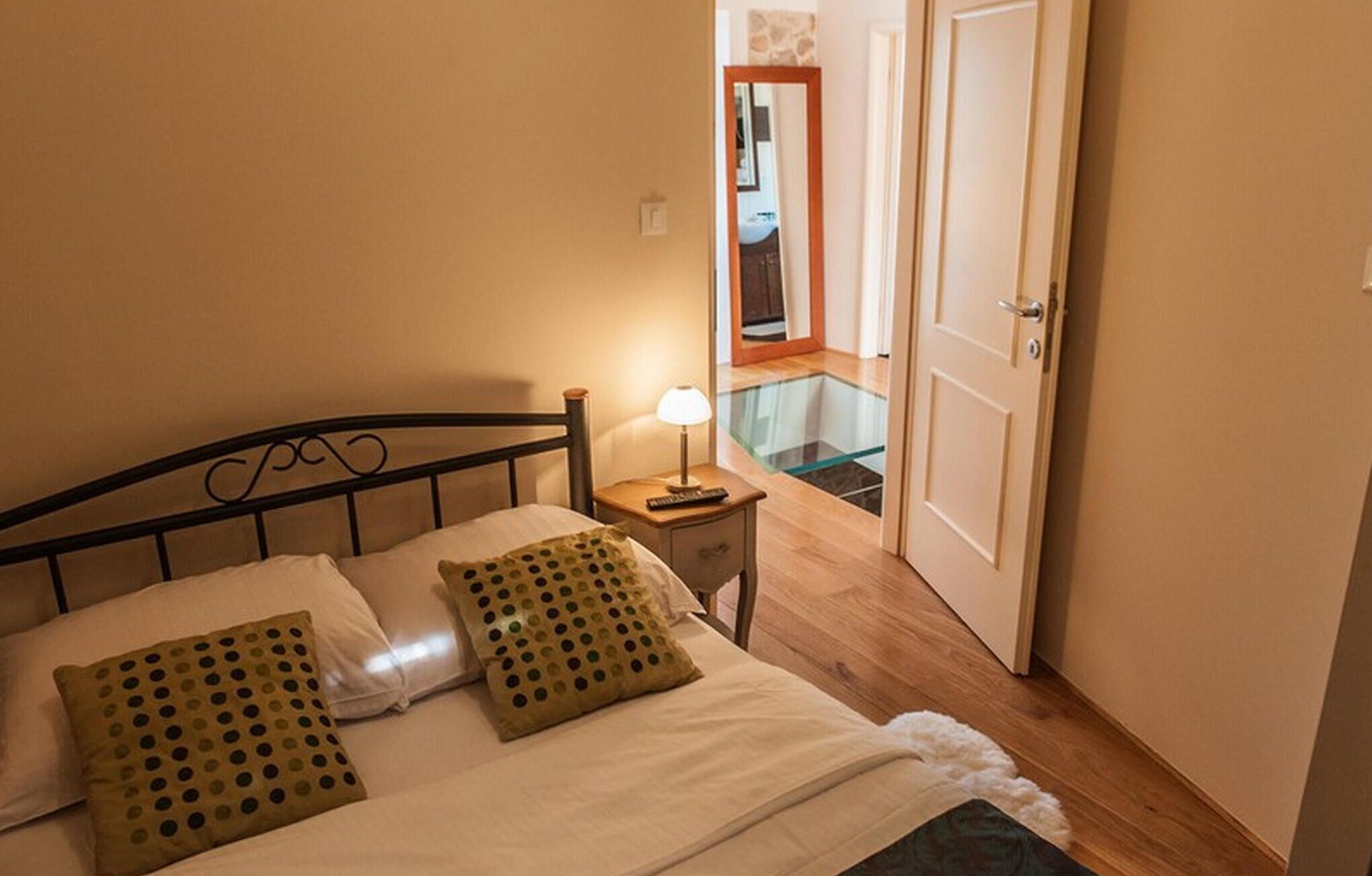 Een netjes opgemaakt bed met witte lakens en twee groene kussens, een bedlampje en een houten nachtkastje.