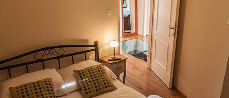 Een netjes opgemaakt bed met witte lakens en twee groene kussens, een bedlampje en een houten nachtkastje.