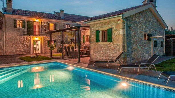 A stone house with a swimming pool, outdoor seating, and a covered patio area.