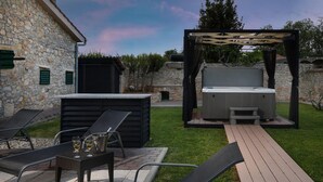 An outdoor patio area with a hot tub, lounge chairs, and a pergola.