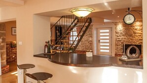 A modern kitchen with a curved island, a staircase, and a stone wall.