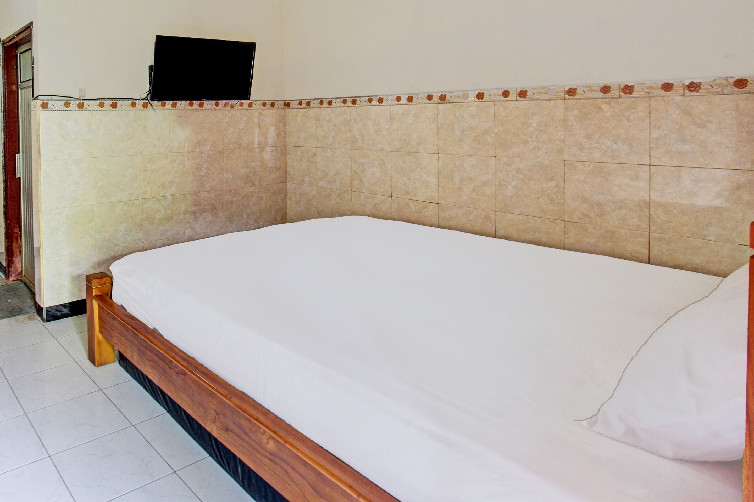 Una cama individual con estructura de madera y ropa de cama blanca en una habitación con paredes de baldosas beige y un detalle decorativo.