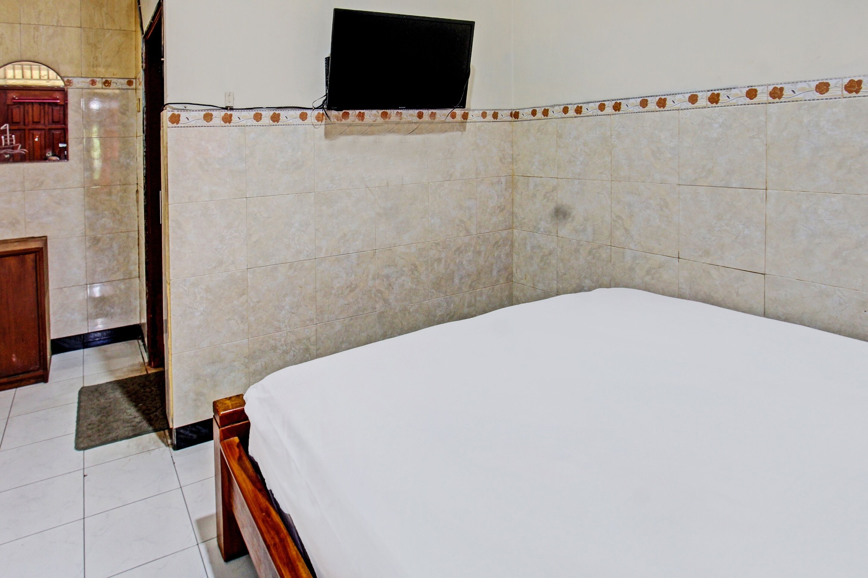 Una habitación de hotel con una cama, un televisor montado en la pared y un armario de madera.