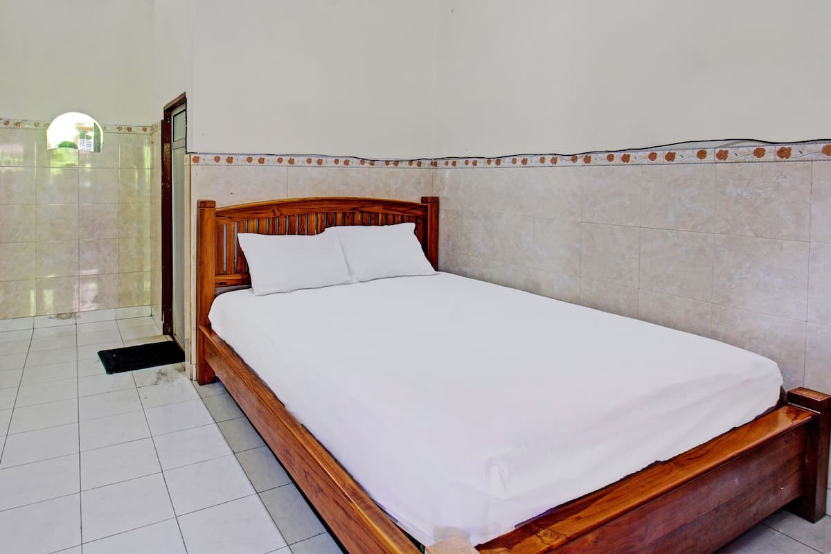 Una cama bien tendida con ropa blanca en una habitación con pisos de baldosas y cabecera de madera.