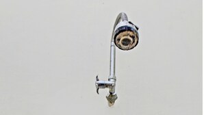 A bathroom with a showerhead mounted on a wall, a faucet, and a visible pipe on the floor. - Hotel O Astri Homestay (Mataram)