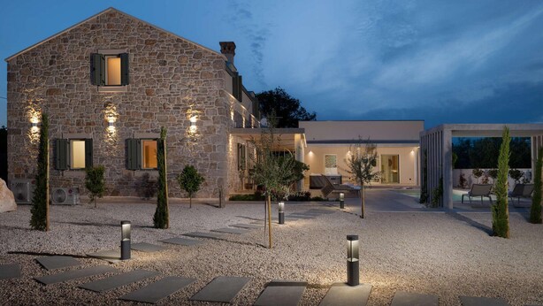 Un edificio de piedra con una extensión moderna, mobiliario exterior y un patio de grava.