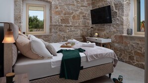 Un dormitorio con pared de piedra, cama con manta blanca y verde, escritorio con lámpara y televisor montado en la pared.