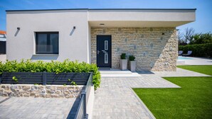 Una moderna casa a due piani con facciata in pietra, una porta d'ingresso nera e un prato curato.