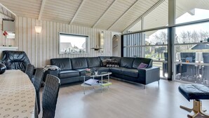 Un vaste salon comprenant un grand canapé d’angle, une table à manger avec des chaises et une porte vitrée donnant sur un espace extérieur.