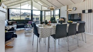 Un vaste espace dédié à la salle à manger, avec un plafond haut, de grandes fenêtres et une cuisine moderne visible au fond.