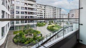 Un edificio moderno con balcón de vidrio, un patio con vegetación y cielo despejado.