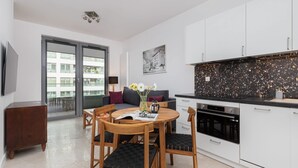 Una cocina moderna con armarios blancos, un salpicadero negro con motas y una zona de comedor con sillas de madera y una mesa.