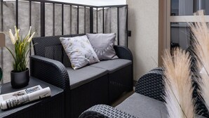 Ein Balkon mit Korbmöbeln, einem Blumentopf und Pampasgras.