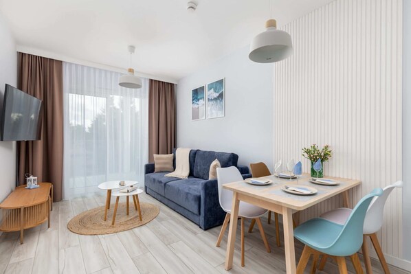 Una sala de estar moderna con un sofá, una mesa de comedor con sillas, un televisor y una ventana con cortinas.