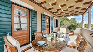 Un patio exterior con mesa de madera dispuesta para comer, rodeado de sillas.