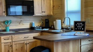 A compact kitchen with wooden cabinets, a built-in microwave, a coffee bar, and a welcome sign for an inlet retreat. - Surf City Family Getaway | Cabin w/ Loft & Pets OK (Holly Ridge)