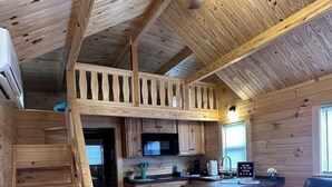 A wooden cabin interior with a kitchen, dining area, and a loft bedroom. - Surf City Family Getaway | Cabin w/ Loft & Pets OK (Holly Ridge)