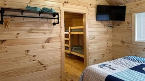 A wooden cabin room with a bed, a TV mounted on the wall, and a closet with a hanging rack. - Surf City Family Getaway | Cabin w/ Loft & Pets OK (Holly Ridge)