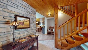 A rustic interior with a stone wall, wooden staircase, and a dining area. - Log Cabin | WiFi | Secluded 5 Acre Lot | Hoskison Hideaway (Angel Fire)