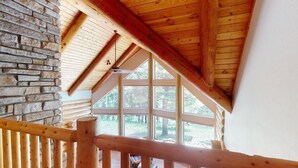 A wooden interior with a stone wall, a wooden staircase, and large windows offering a view of the outdoors. - Log Cabin | WiFi | Secluded 5 Acre Lot | Hoskison Hideaway (Angel Fire)